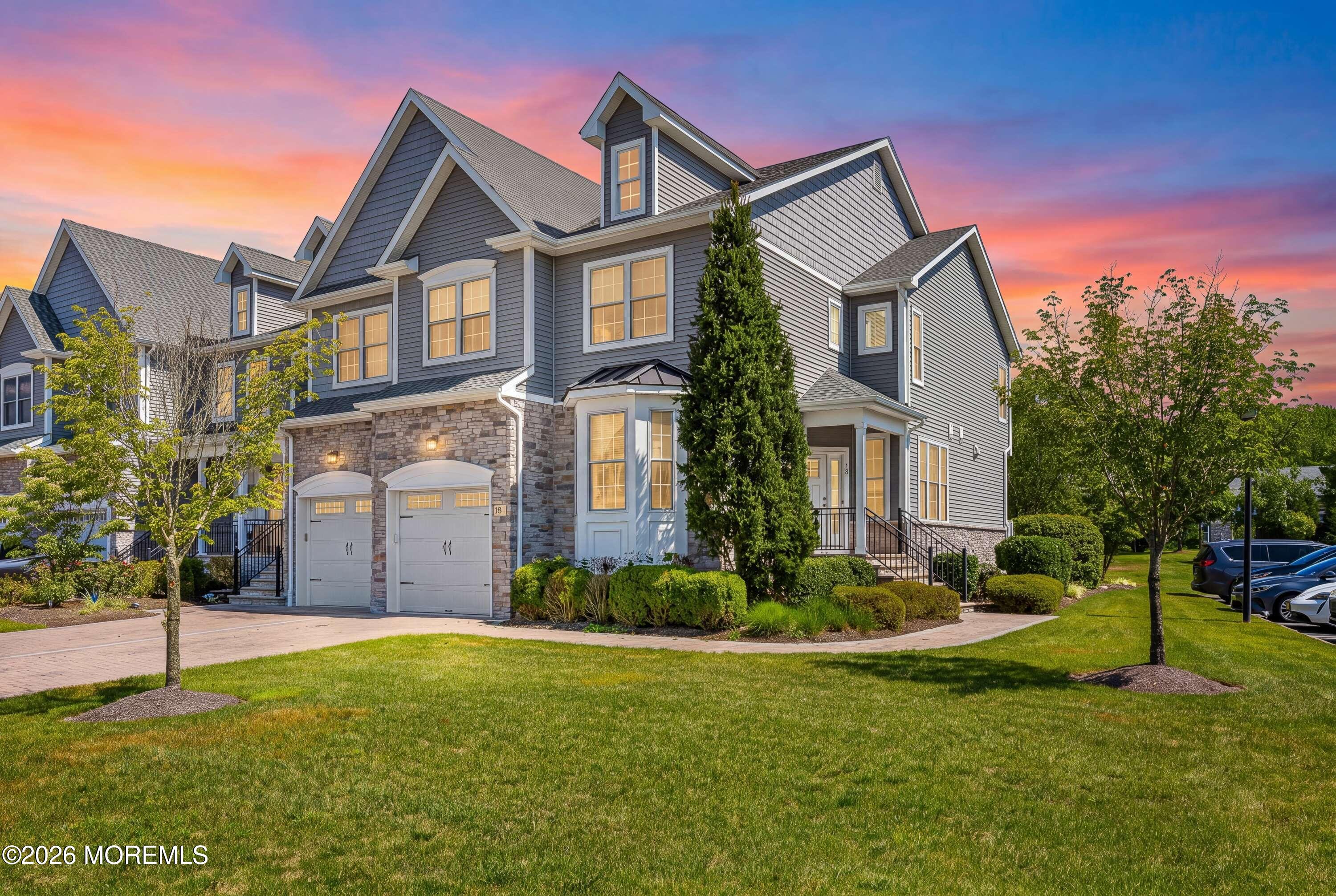 Gray multi-story home with stone facade, two garages, and landscaped lawn at sunset.