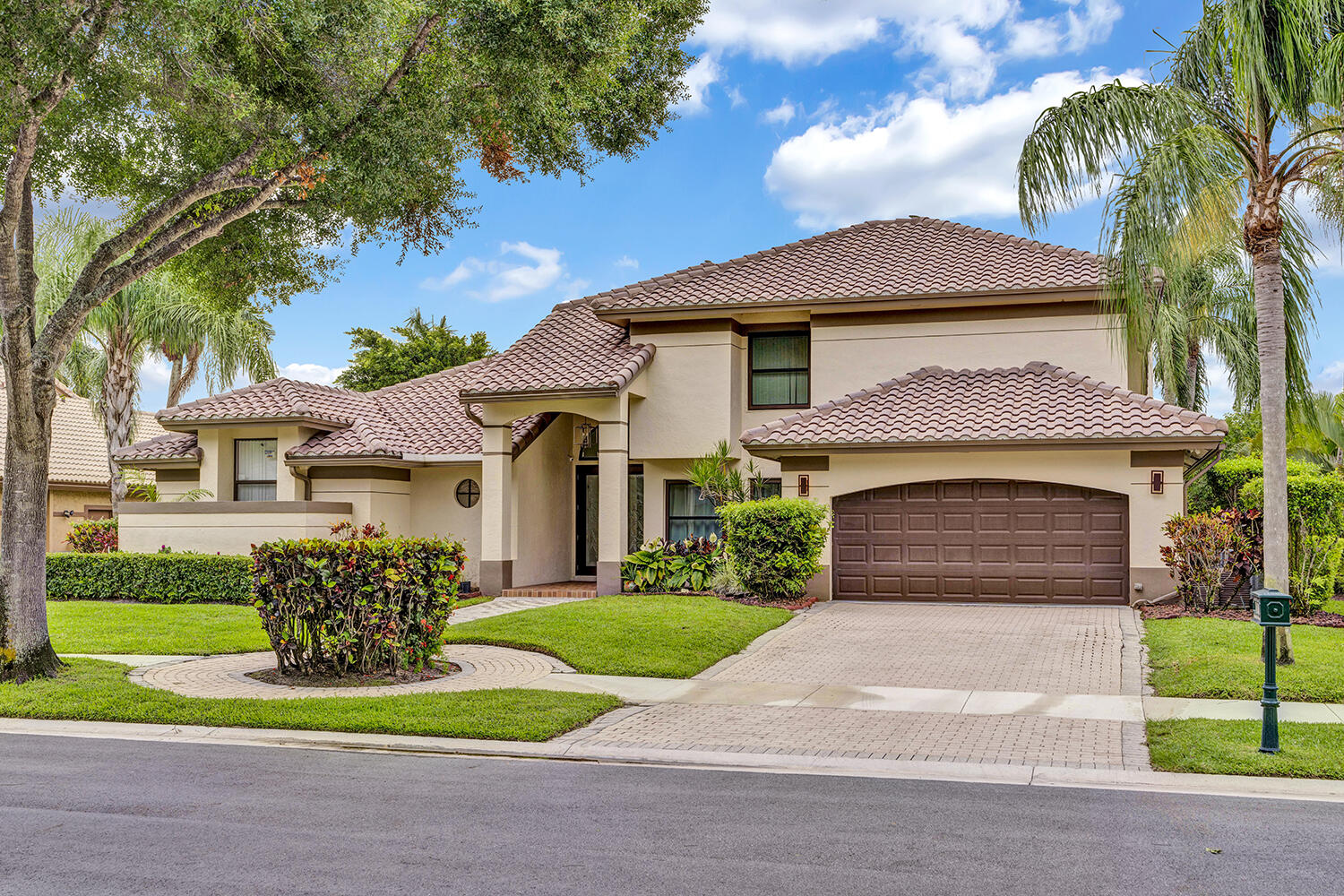 Two-story stucco home with a terracotta tile roof, double garage, landscaped lawn, and palm trees.
