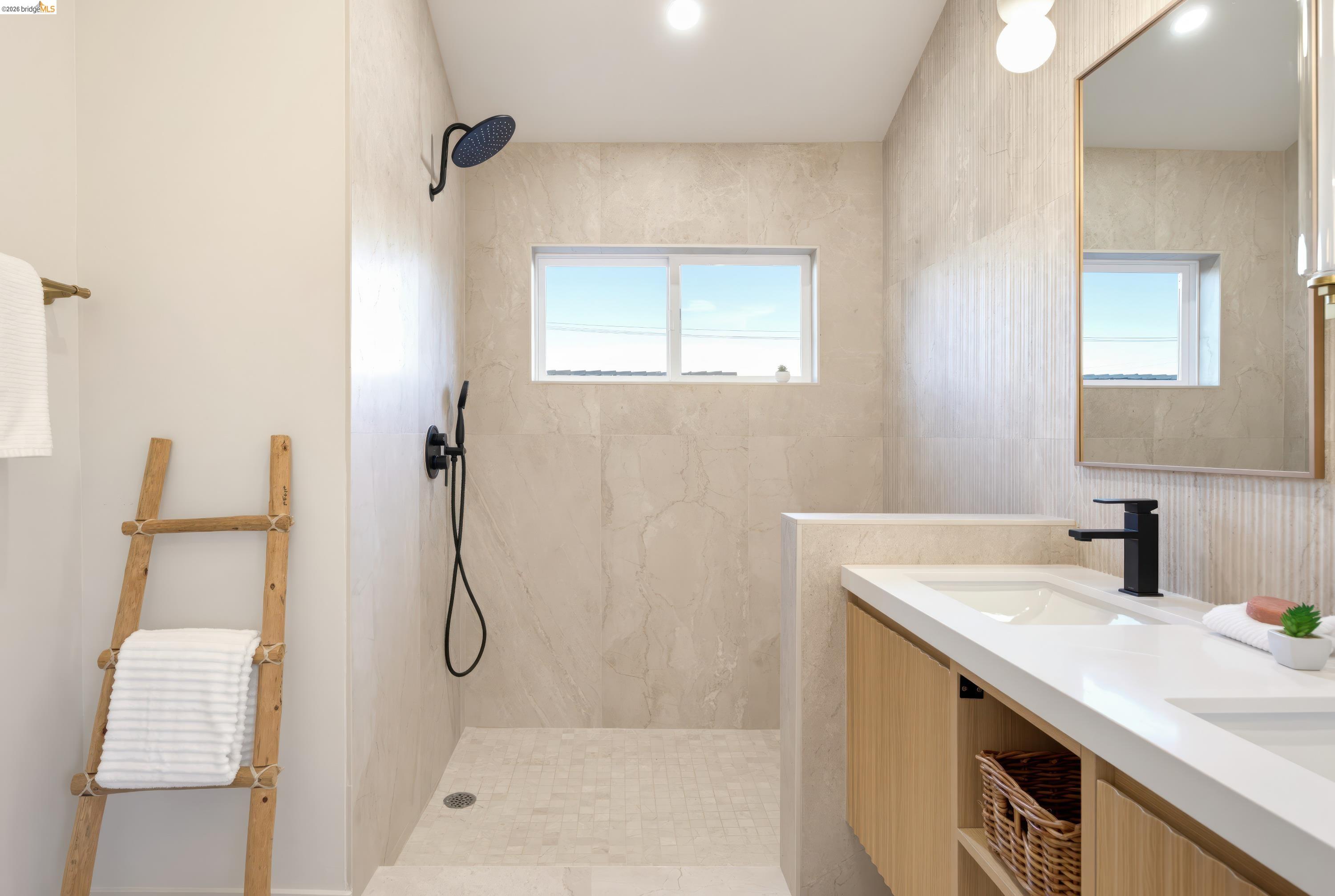 Bathroom with a tiled walk-in shower, bright window, and long double-sink vanity.