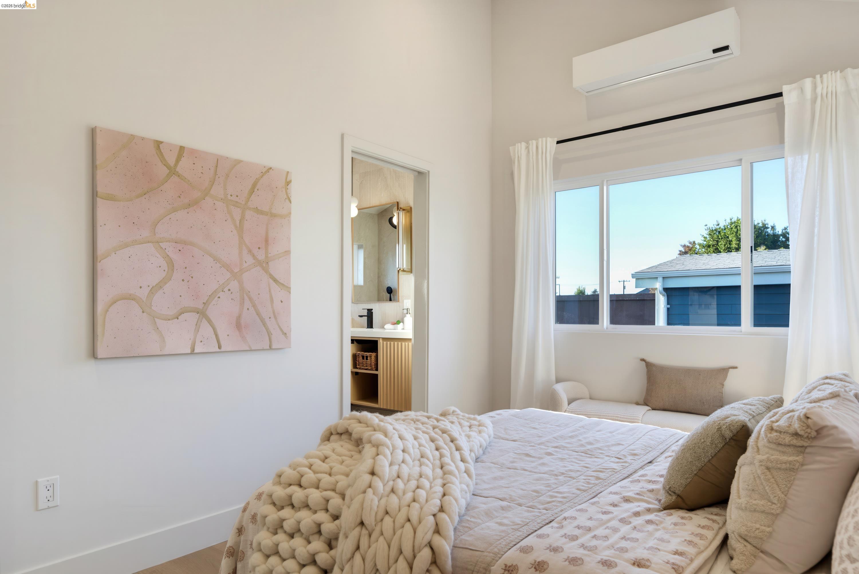 Bedroom with cream knit bedding, abstract pink wall art, and a large curtained window.