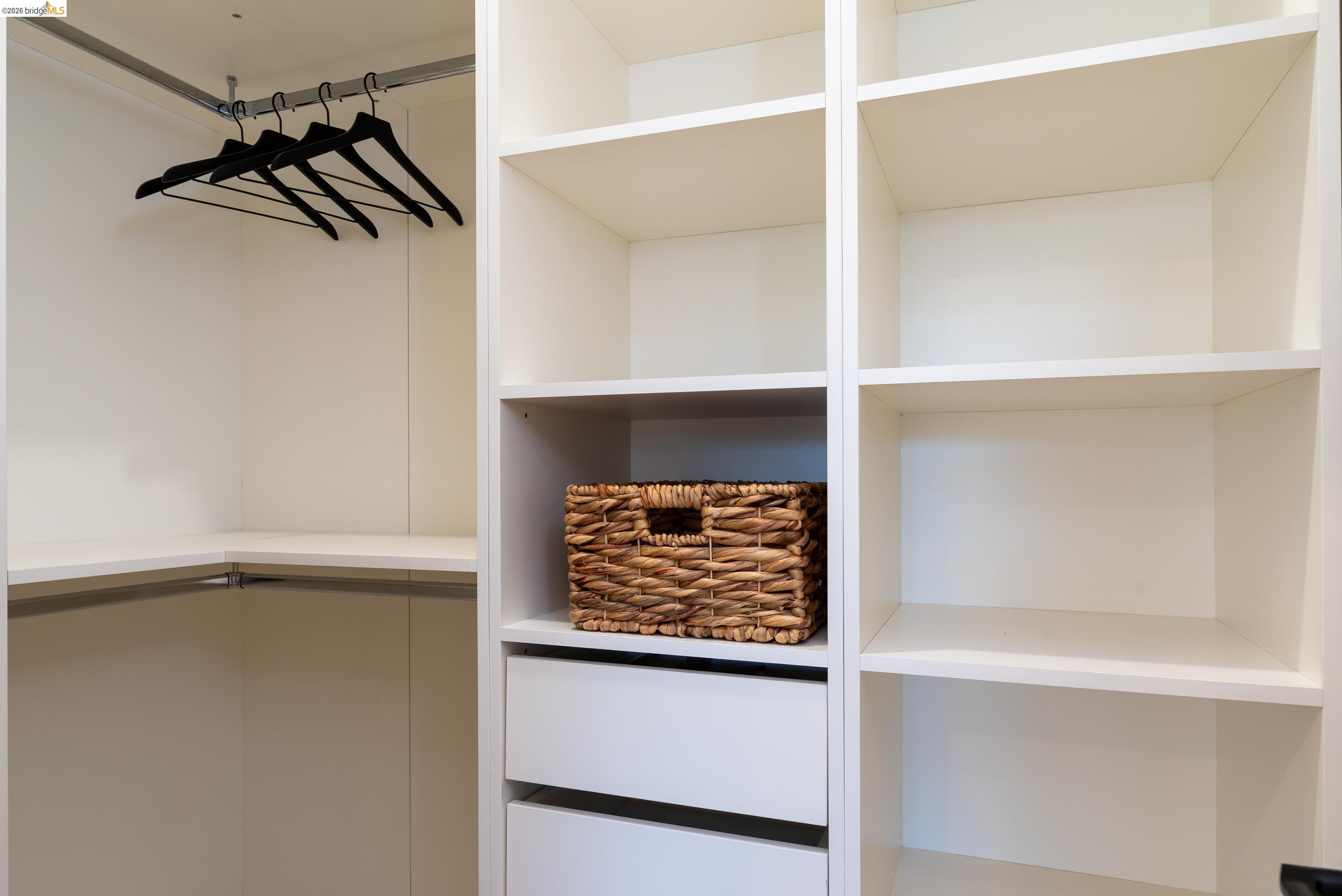 Walk-in closet with built-in shelves, drawers, black hangers, and a woven basket.