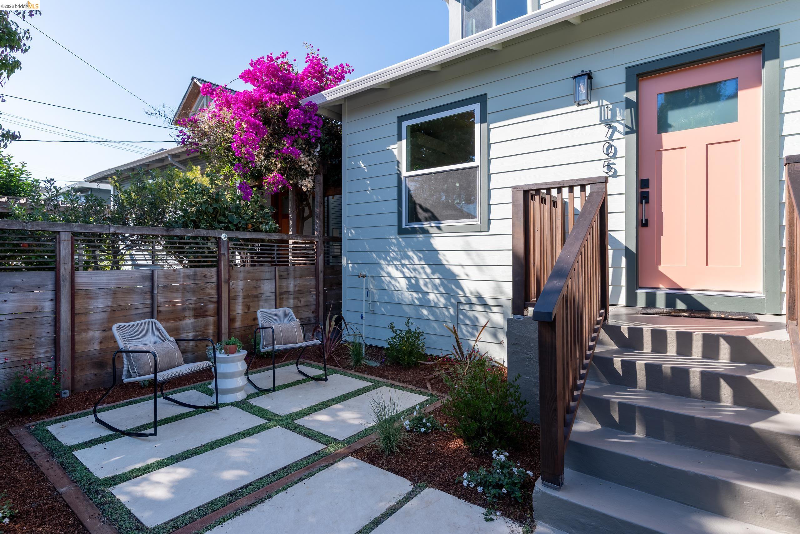 Light blue home with a pink front door, patio chairs, and blooming bougainvillea.