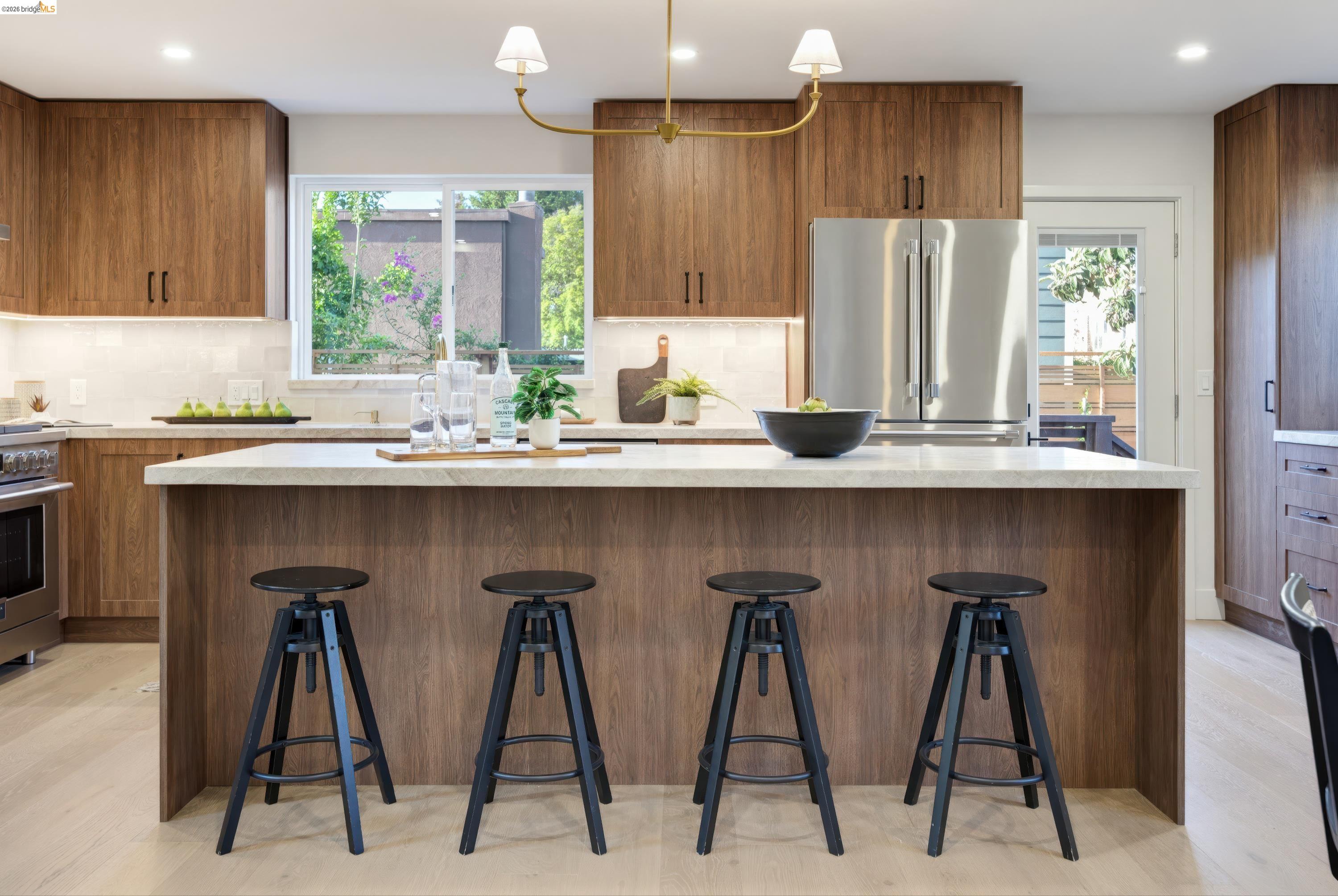 Kitchen with a large wood island, four black stools, and stainless steel refrigerator.