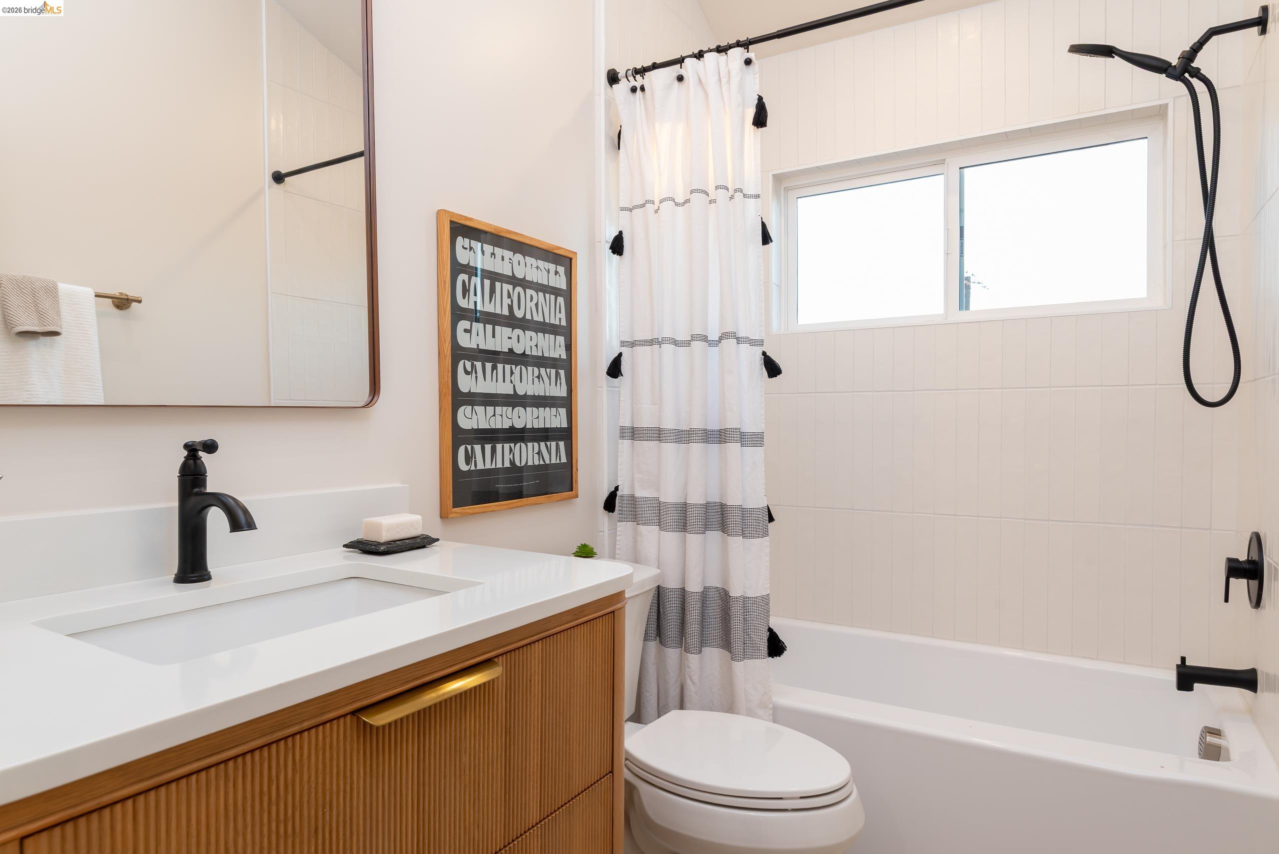 Bathroom with a ribbed wood vanity, black fixtures, and a tiled tub with a window.