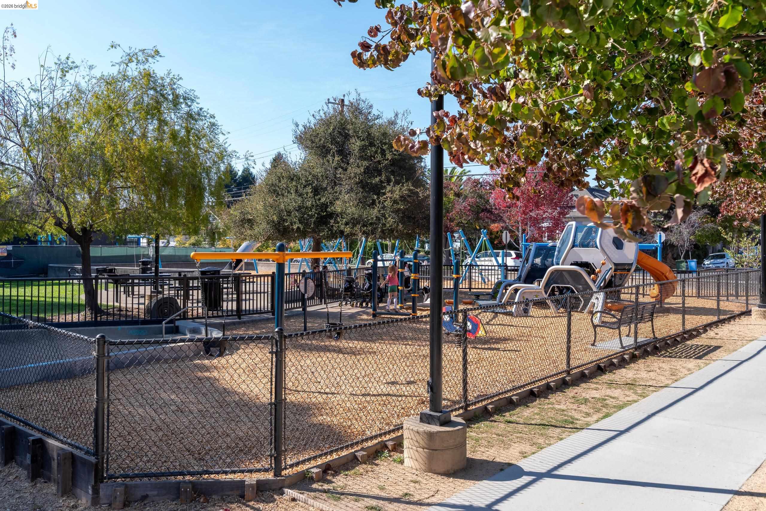 Neighborhood playground with colorful climbing equipment and slides behind a chain-link fence.