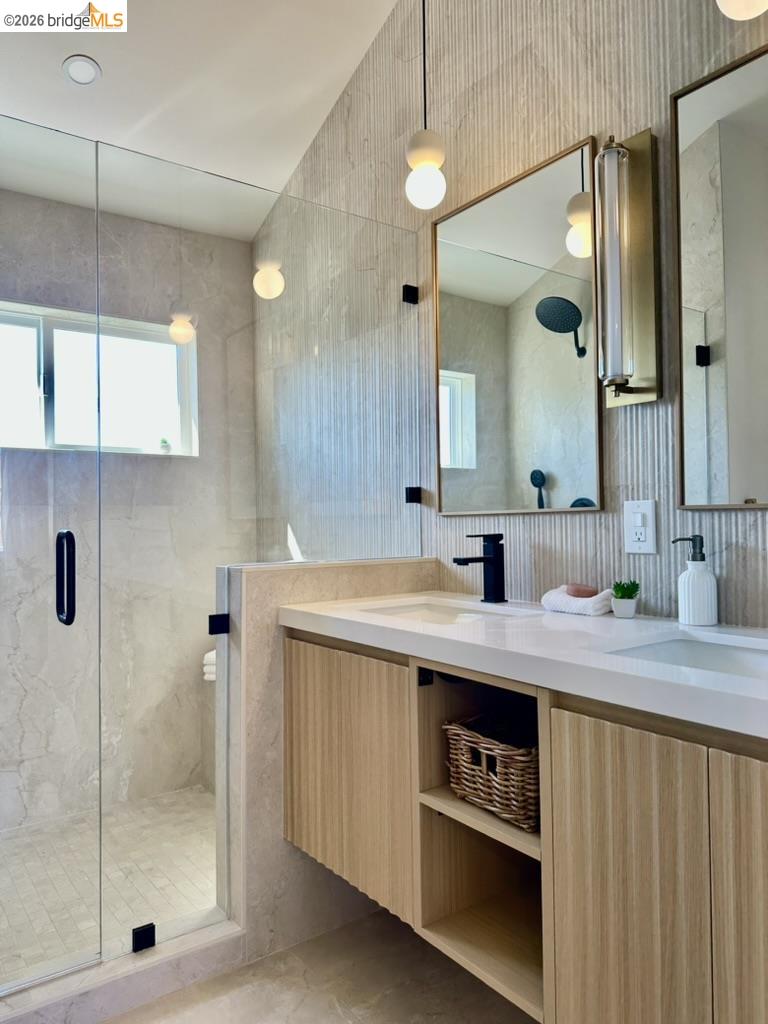 Modern bathroom with a glass shower and pale stone tile beside a wood vanity.