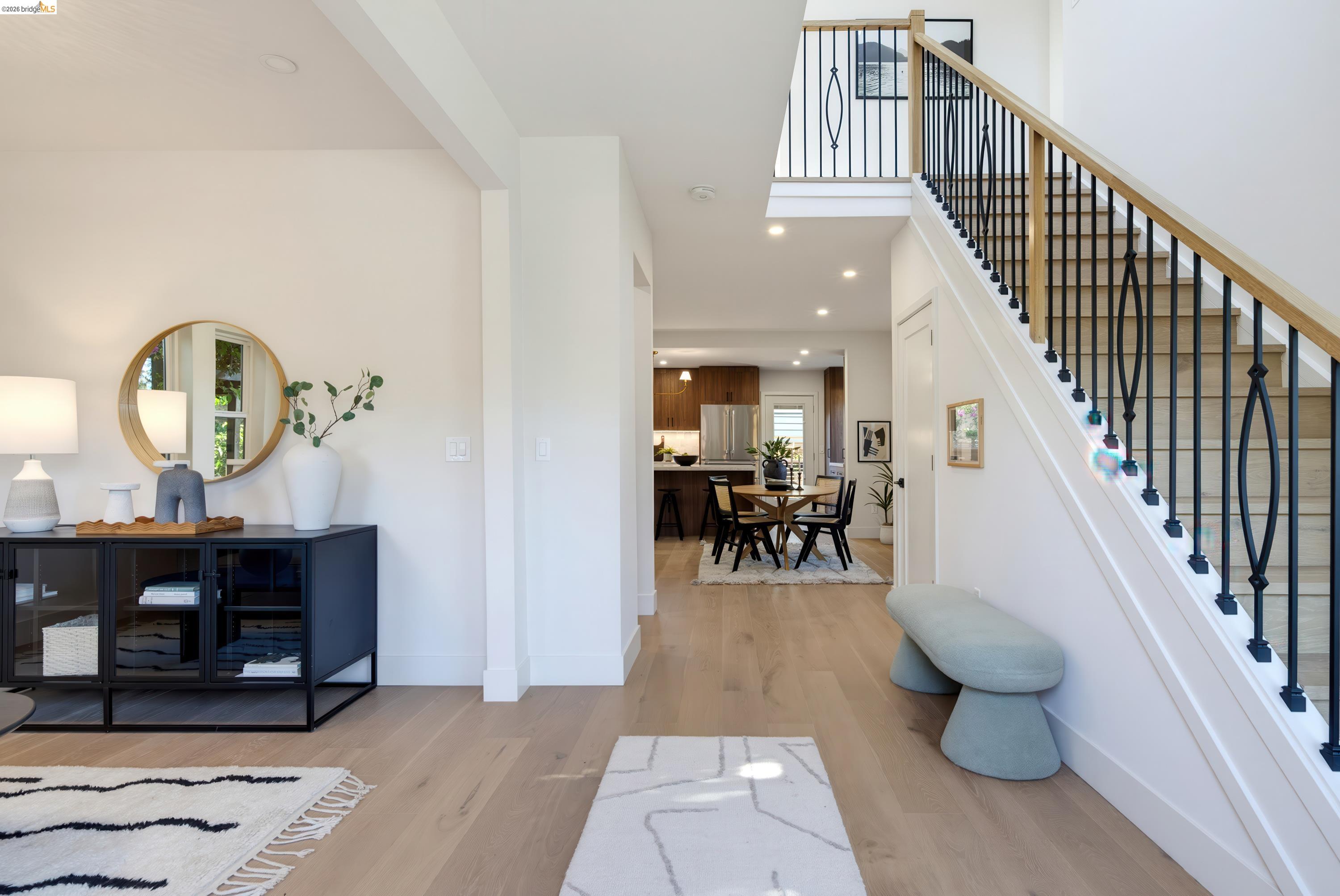 Staged entryway with pale wood floors, a black console, and a staircase with black metal railings.