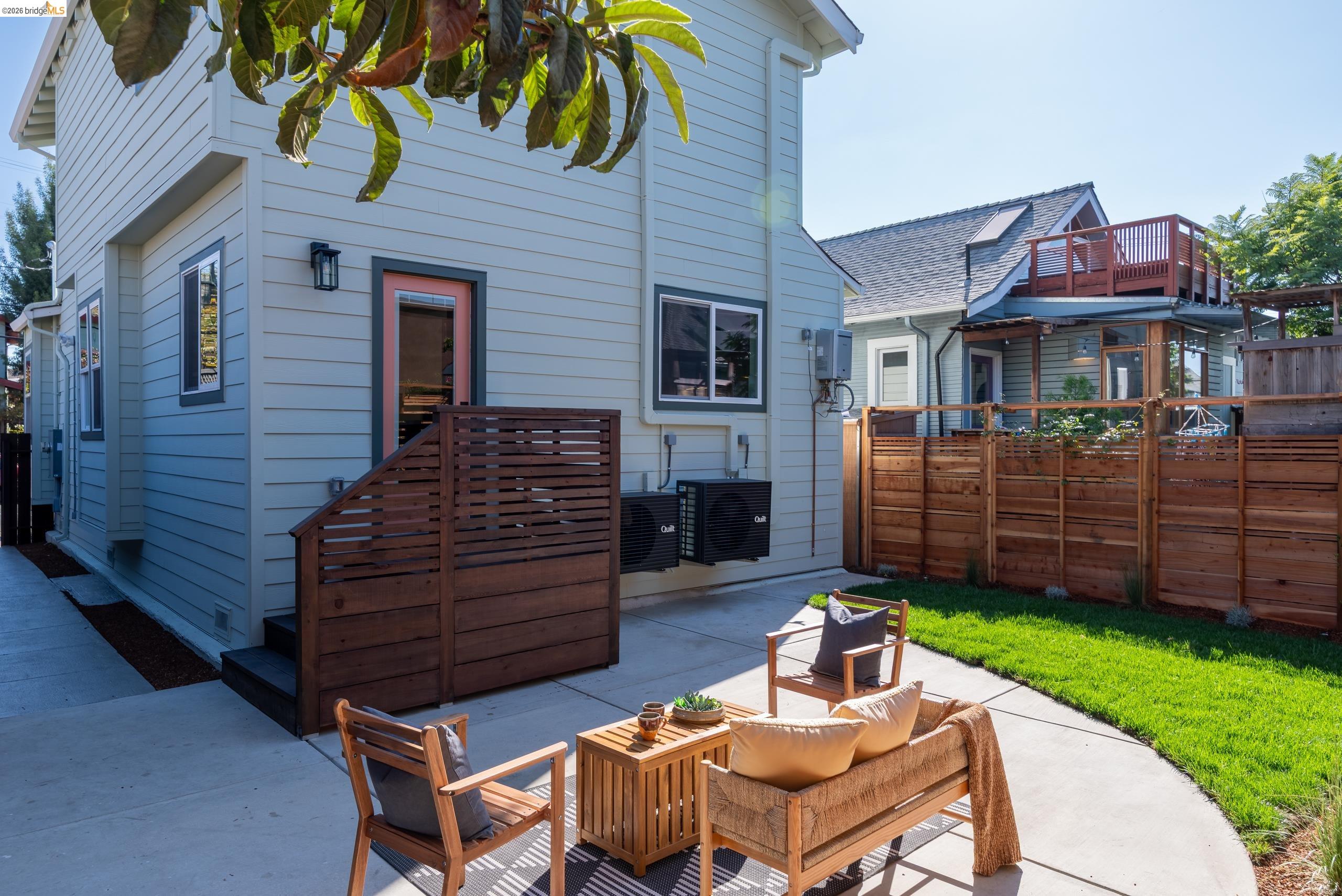 Home’s backyard patio with wood seating, a green lawn, and a tall privacy fence.