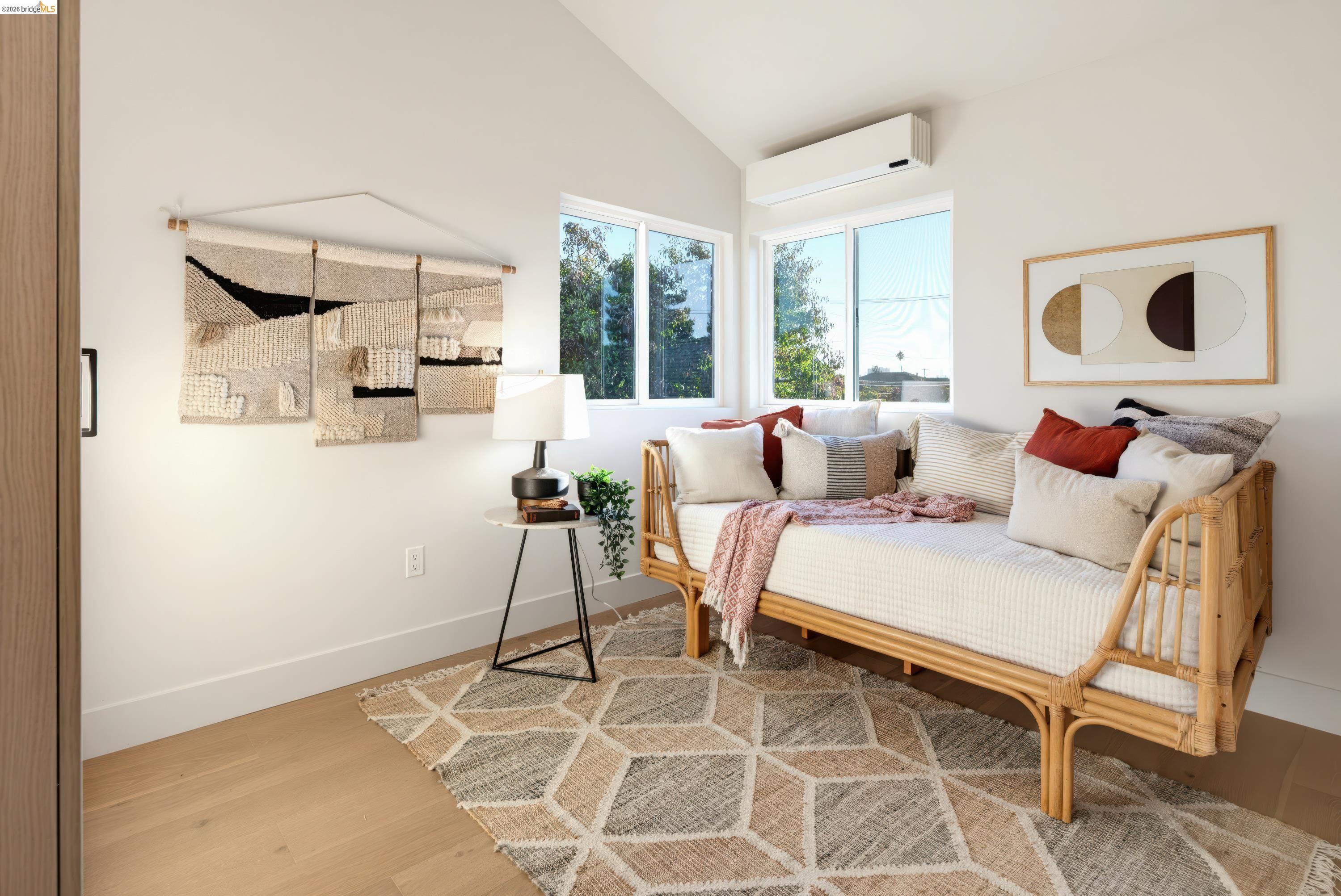 Bedroom with a rattan daybed, geometric rug, woven wall hanging, and large windows.