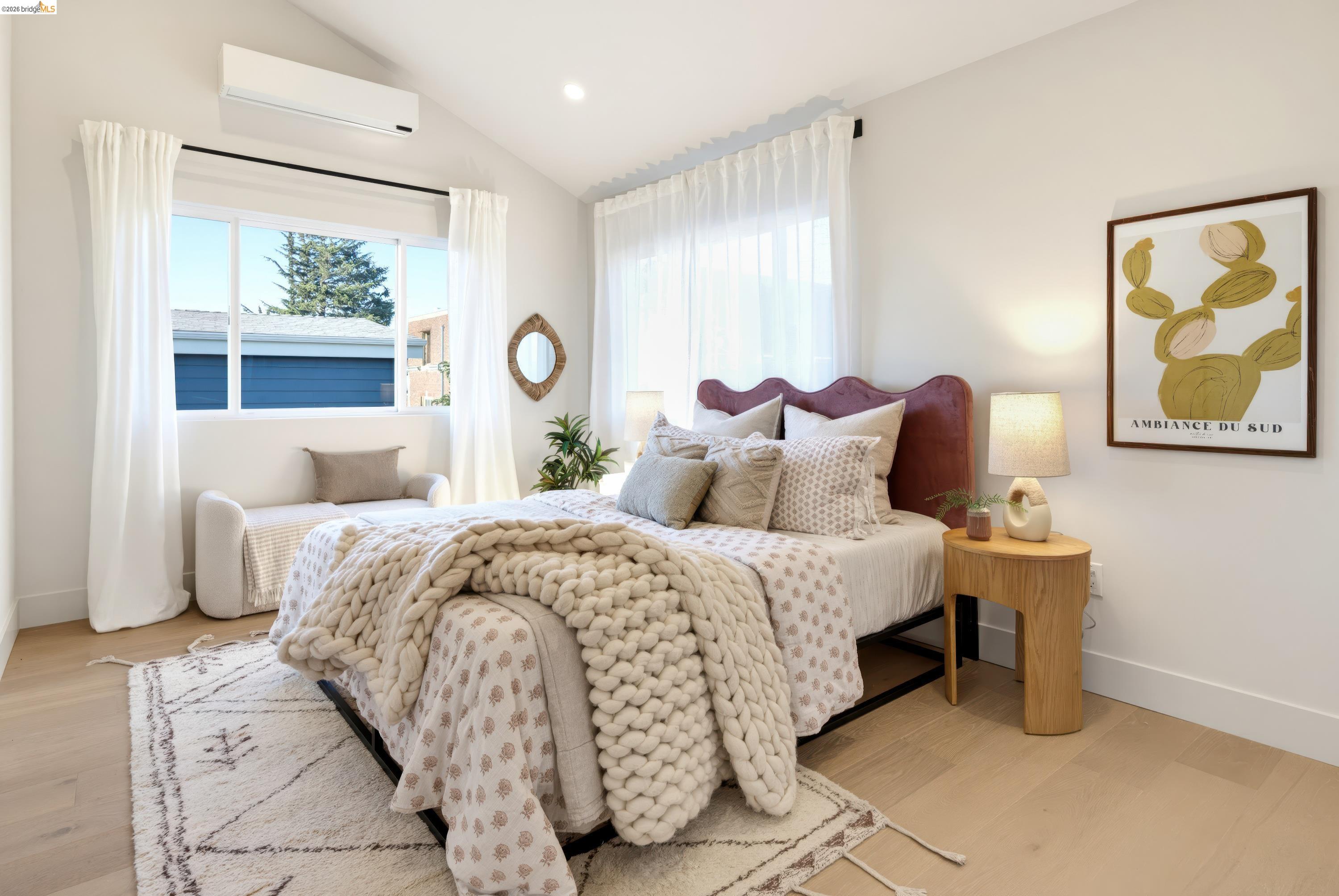 Staged bedroom with a chunky knit blanket, mauve headboard, and bright curtained windows.