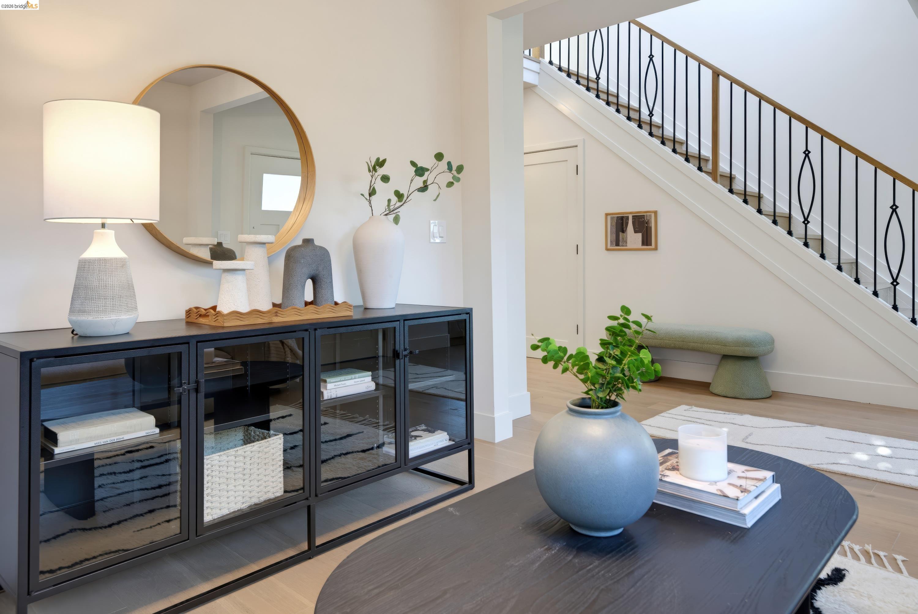 Staged entry with a black glass-front console and round mirror beside a staircase with a black metal railing.