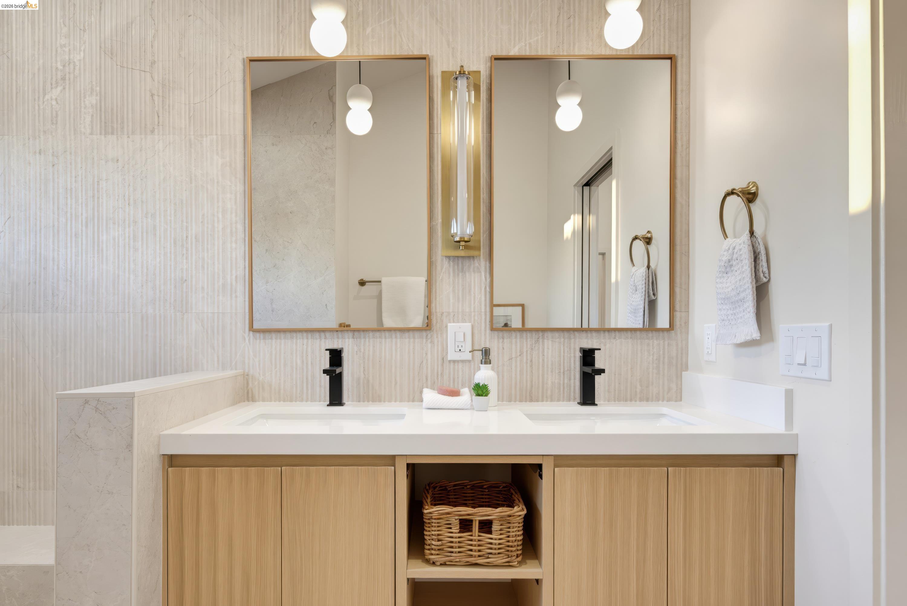 Bathroom with a double-sink vanity, light wood cabinets, and brass-framed mirrors
