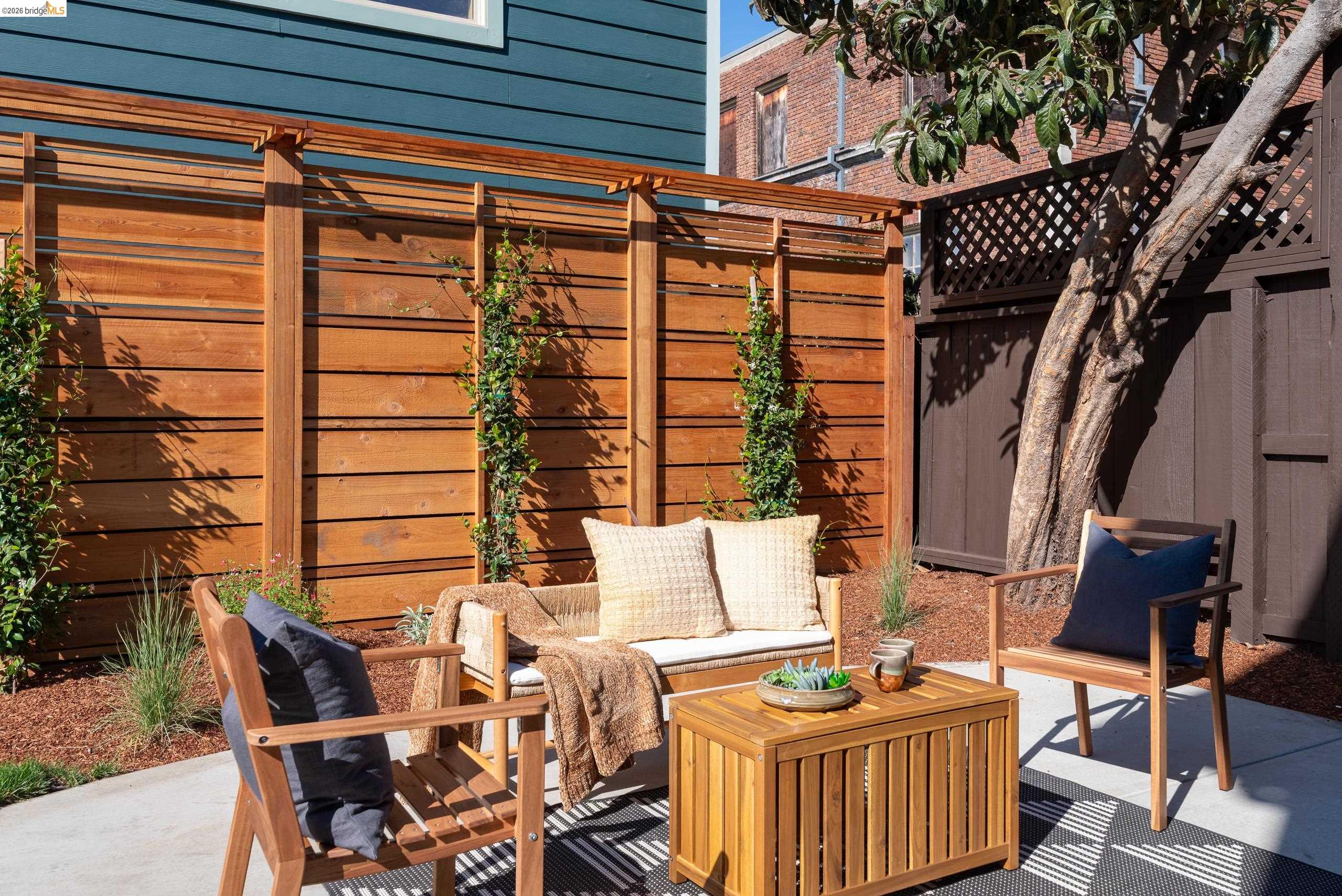 Furnished patio with wooden seating, a cedar privacy fence, and a mature tree.