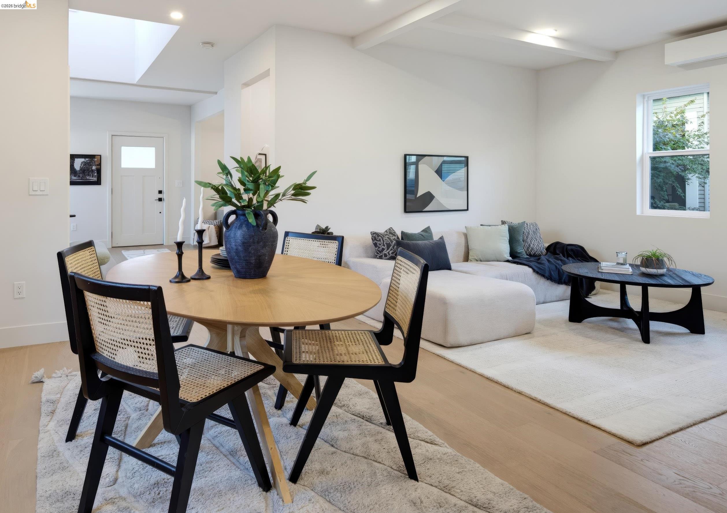 Open-plan living and dining room with a round wood table, white sectional, and skylight.