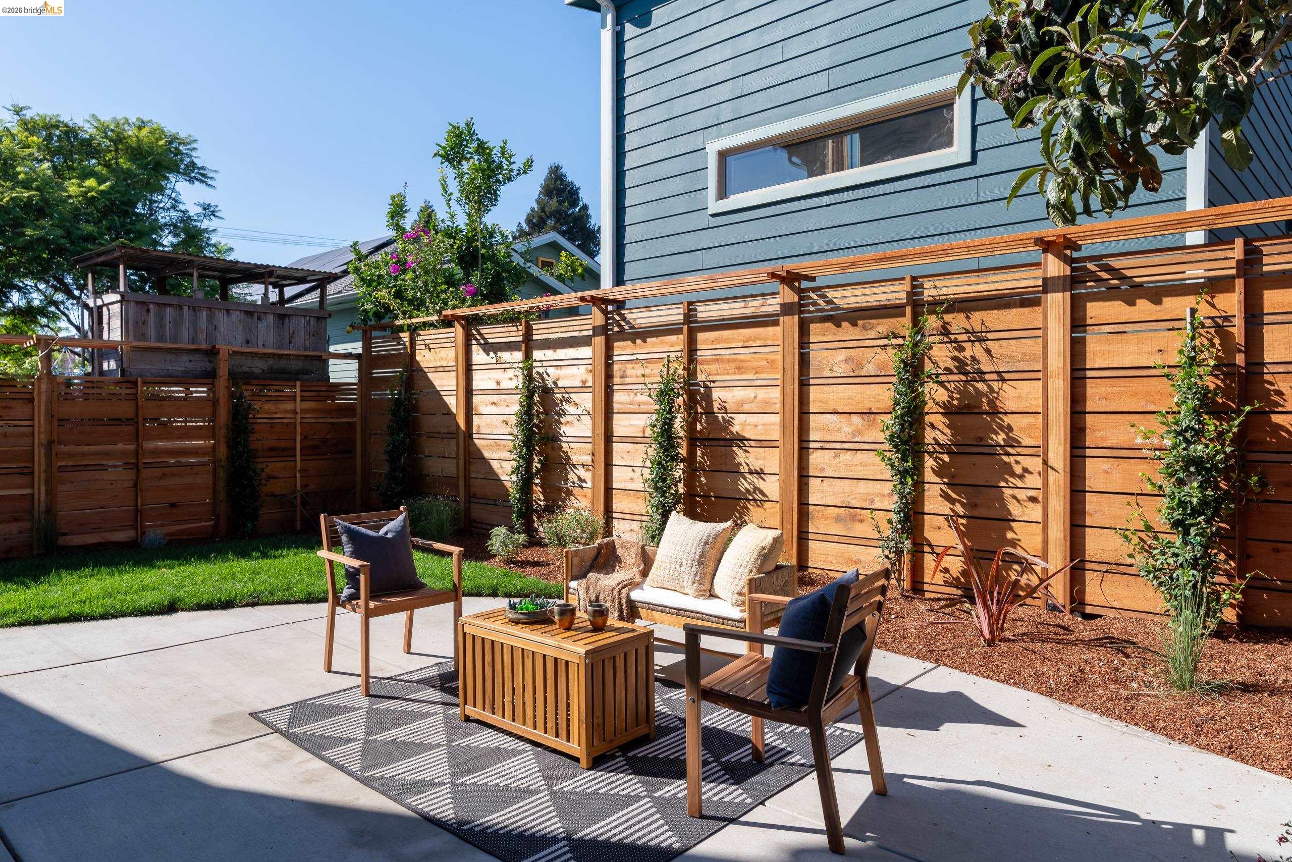 Backyard patio with wood-fenced seating area, outdoor furniture, small lawn, and planted beds.