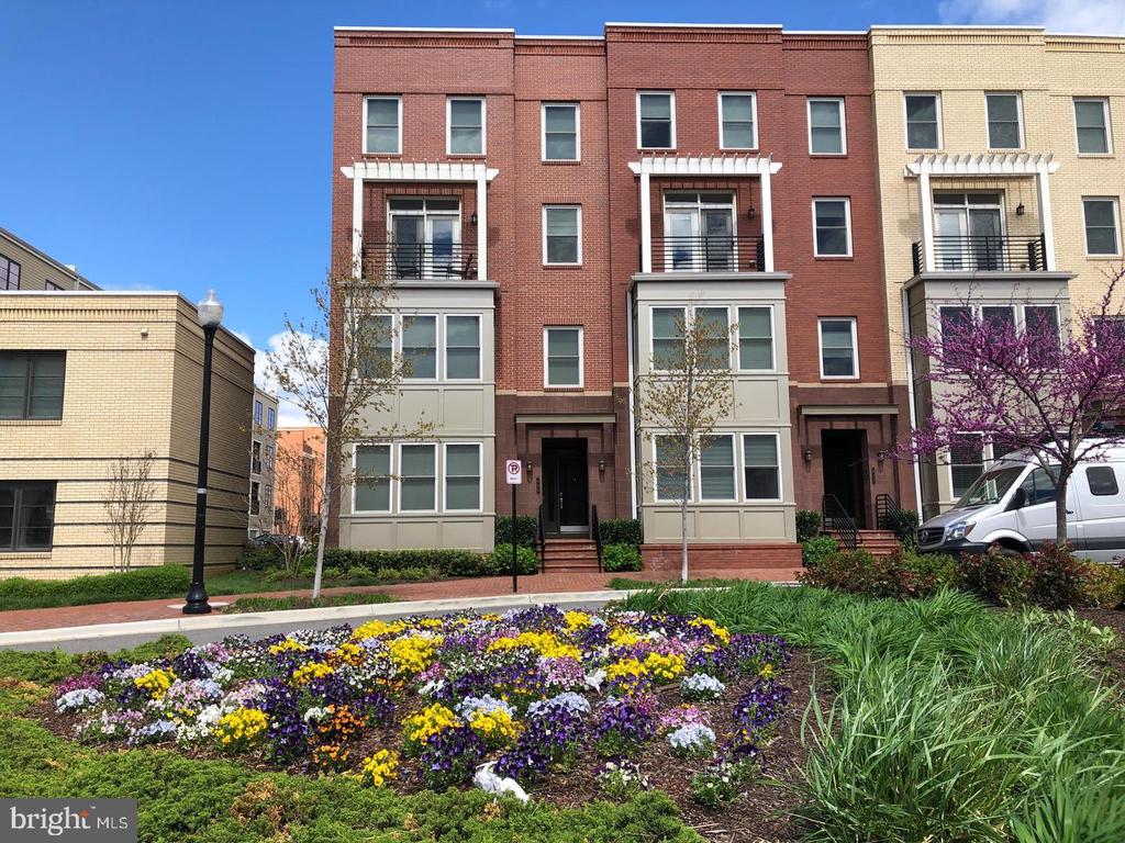 Brick townhouses with balconies behind a colorful flower bed and flowering tree.