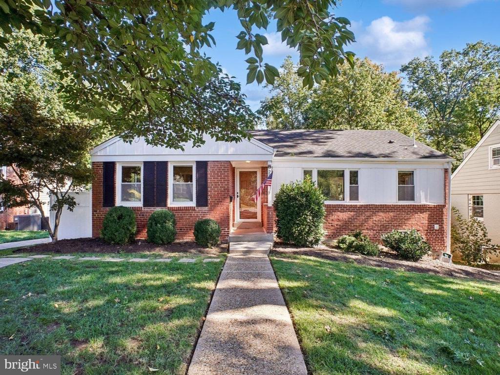 Single-story brick and white-sided home with dark shutters, a front walkway, and mature trees.