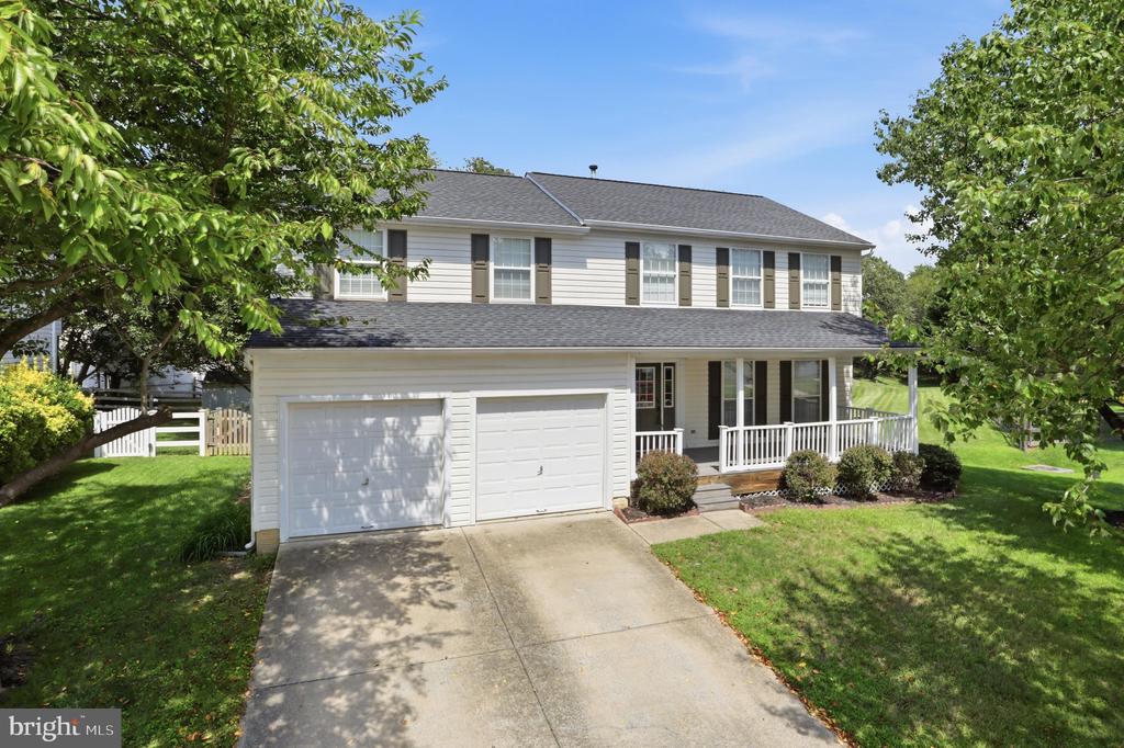 Two-story house with a two-car garage and covered porch, framed by leafy trees.