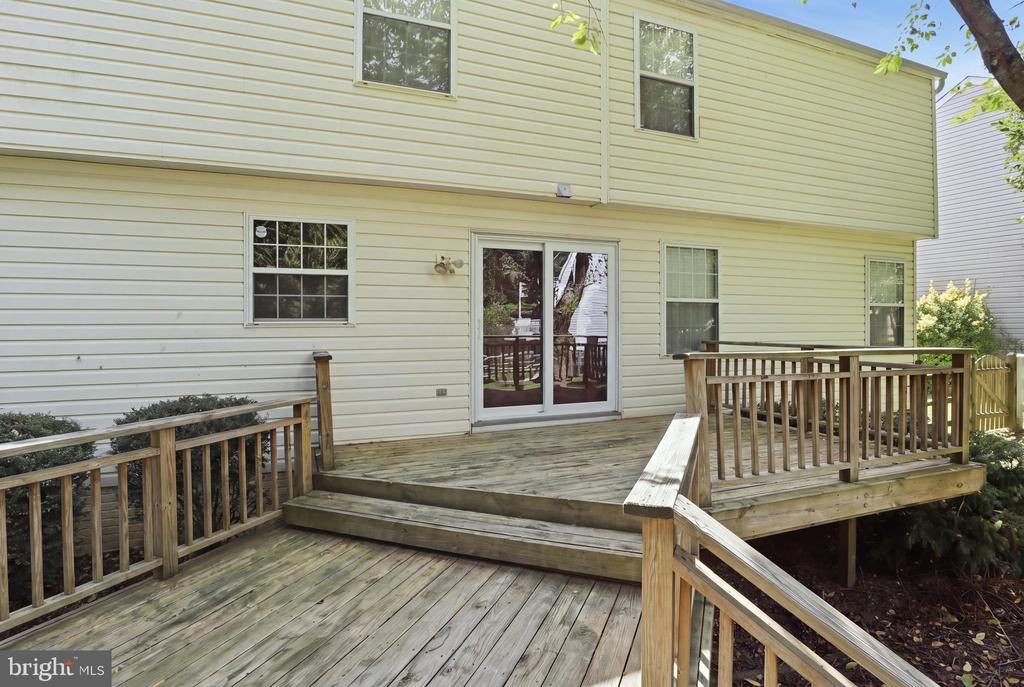 Rear of a two-story house with a raised wooden deck, broad stairs, and sliding glass doors.