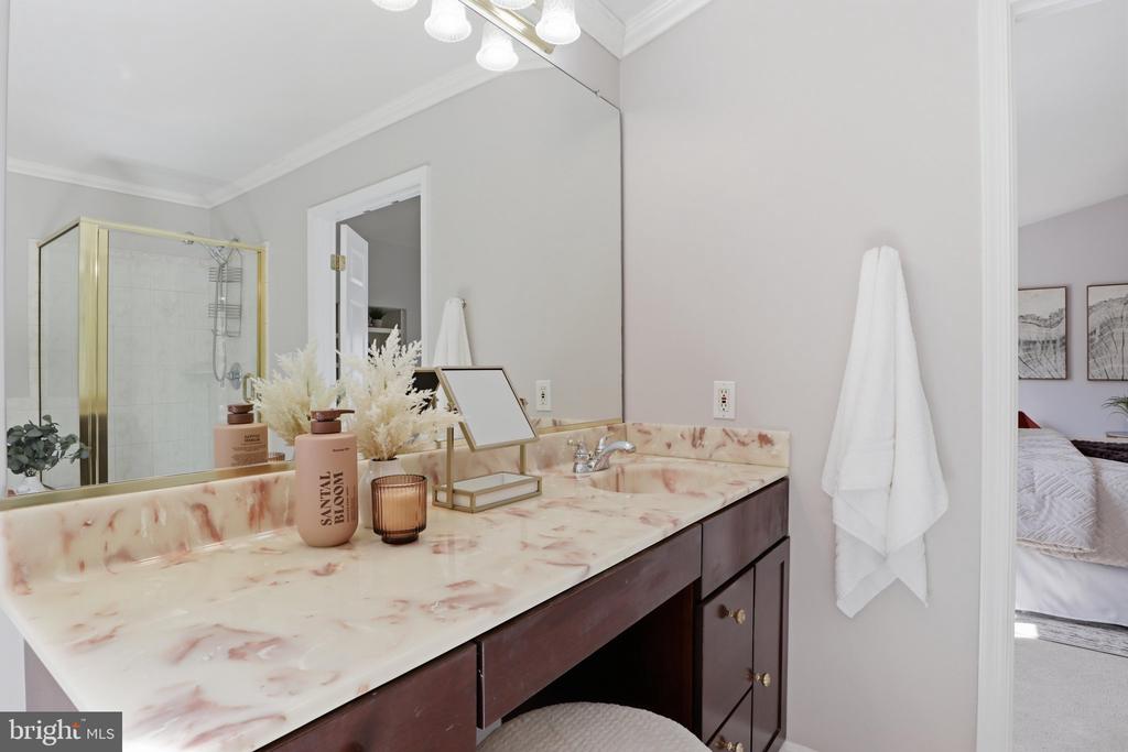 Bathroom vanity with a pink marble-look counter and a brass-trimmed glass shower.