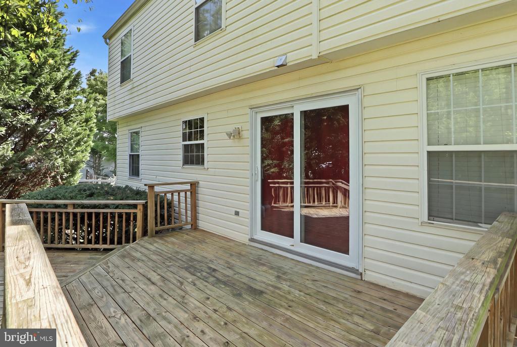 Rear wooden deck with railings beside sliding glass doors on a light-sided home.