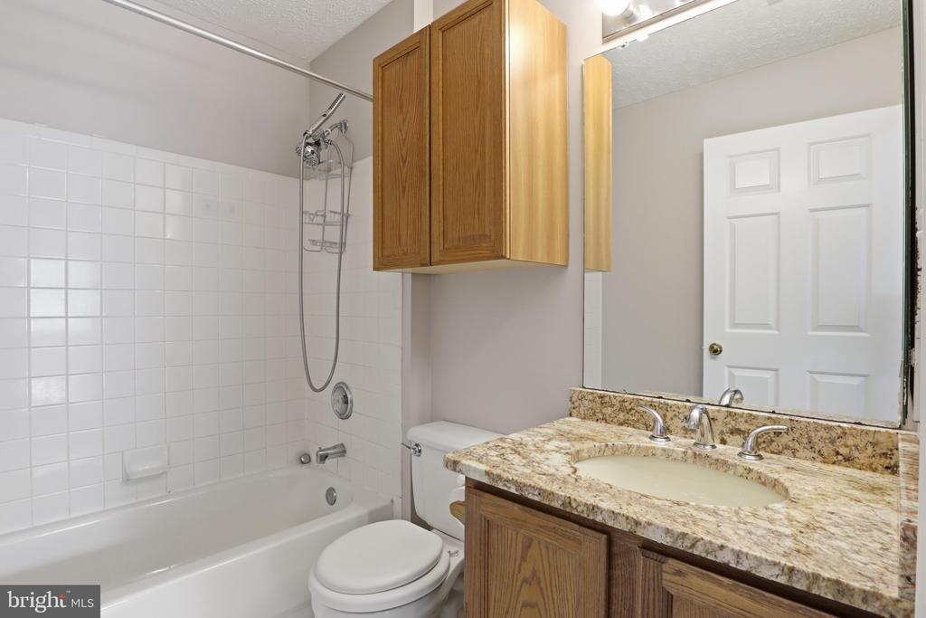 Bathroom with a tiled tub and shower, wood cabinets, and a granite vanity.