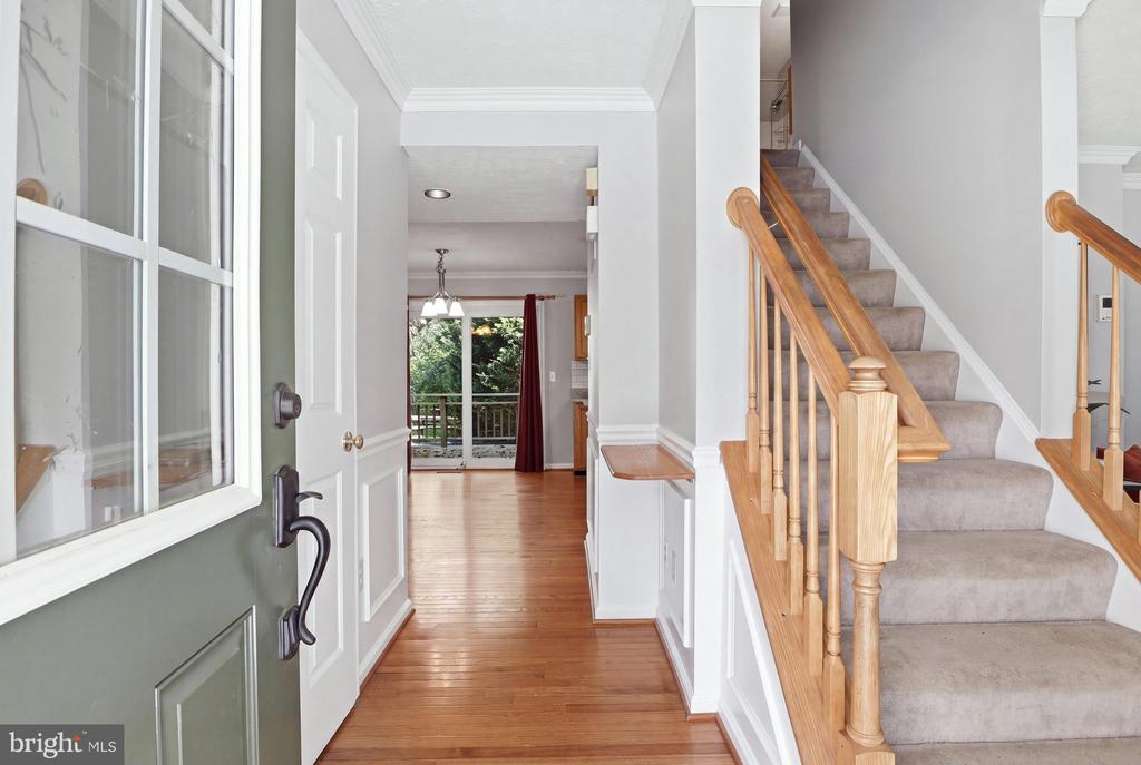Entry foyer with hardwood floors and a carpeted staircase beside the open front door.