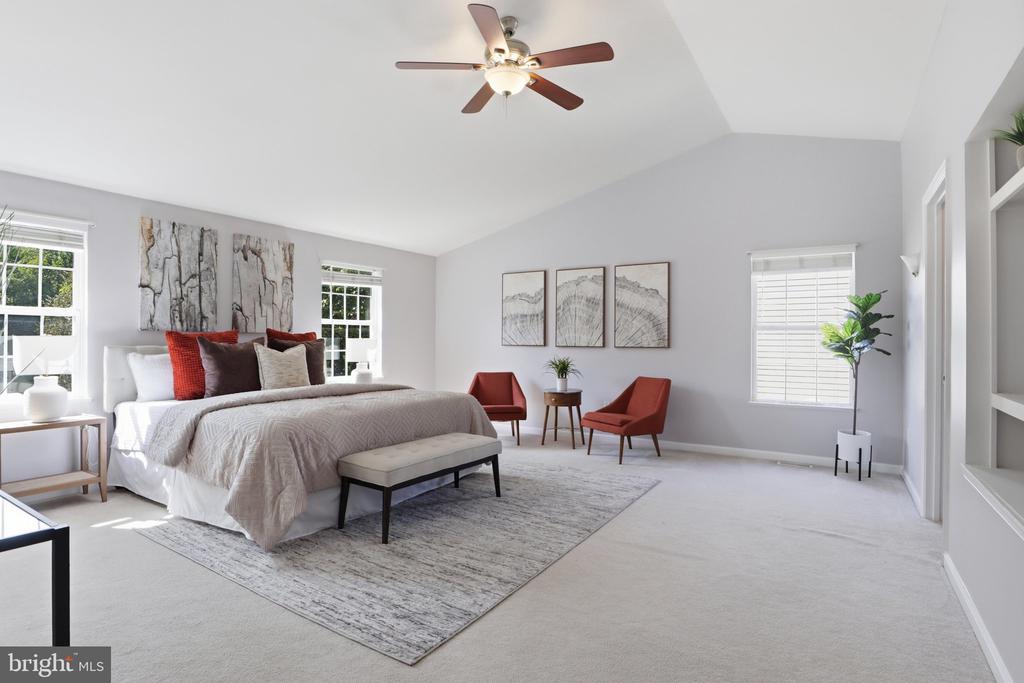 Spacious bedroom with a king-size bed, red accent chairs, large windows, and a ceiling fan.