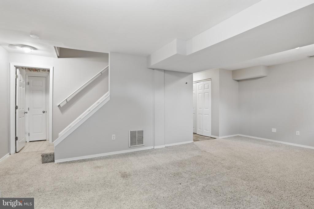 Finished basement room with light carpet, gray walls, and a staircase.