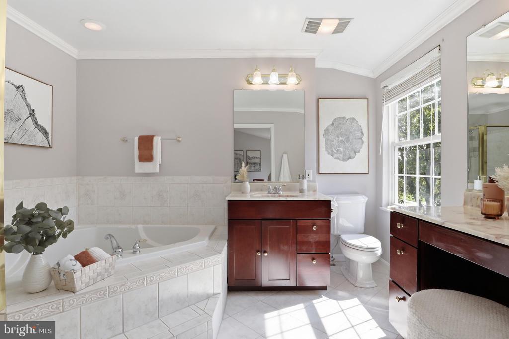 Bathroom with tiled soaking tub, dark wood vanities, and a large sunlit window.