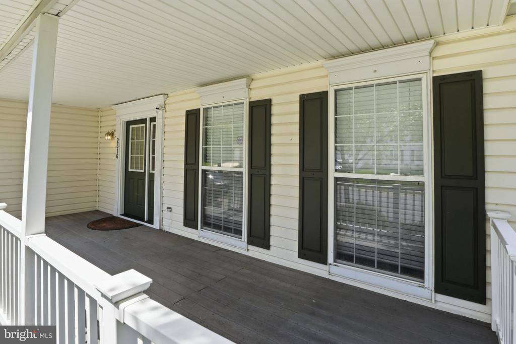 Covered front porch with dark shutters, large windows, and white railings.