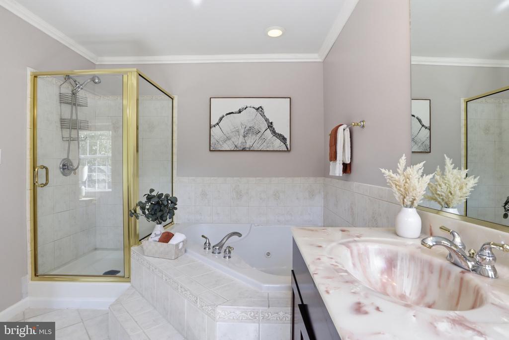 Bathroom with a corner soaking tub, marble vanity, and gold-framed glass shower.