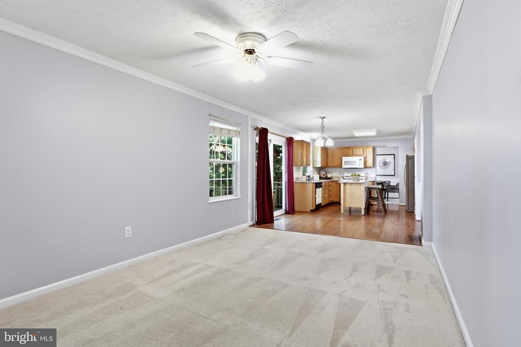 Carpeted living room opening to a kitchen with wood cabinets and a breakfast bar.