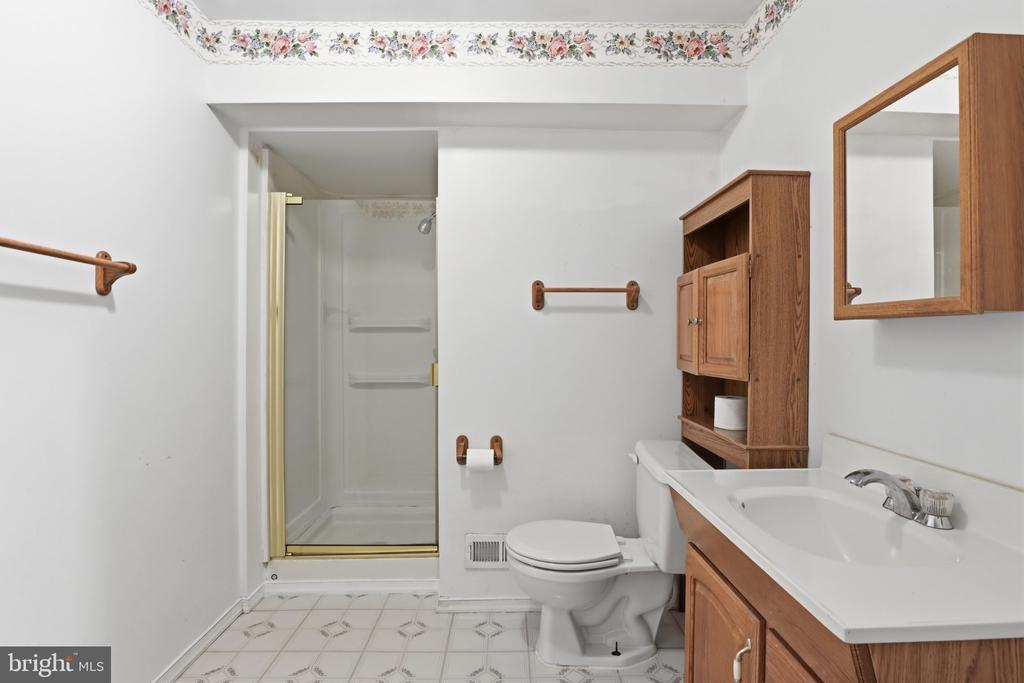 Bathroom with a glass shower, wood vanity, and floral wallpaper border.
