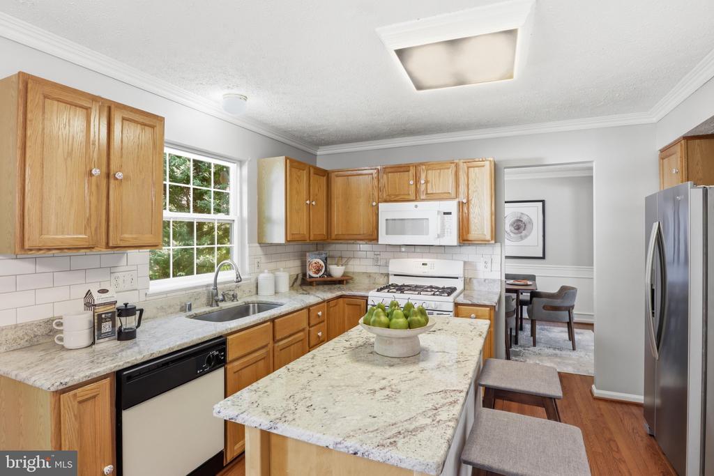 Kitchen with wood cabinets, granite island, stainless steel appliances, and a dining area beyond.