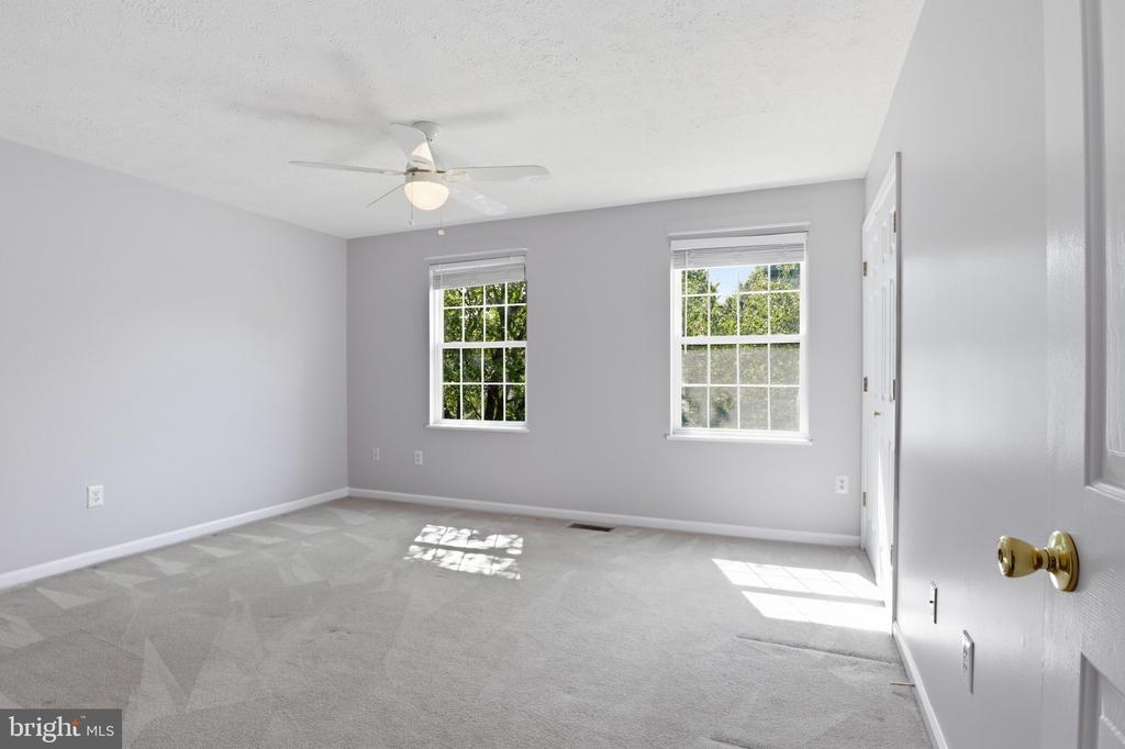 Empty carpeted room with two windows and a ceiling fan.