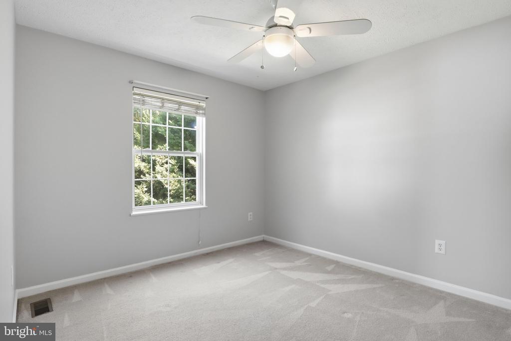 Empty bedroom with beige carpet, a window overlooking greenery, and a ceiling fan.