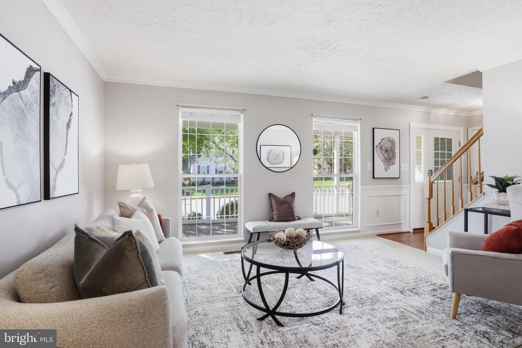 Staged living room with a glass coffee table, large windows, and a wooden staircase.