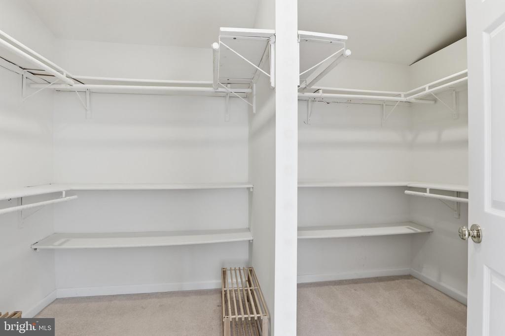 Walk-in closet with white built-in shelves and hanging rods on three walls.