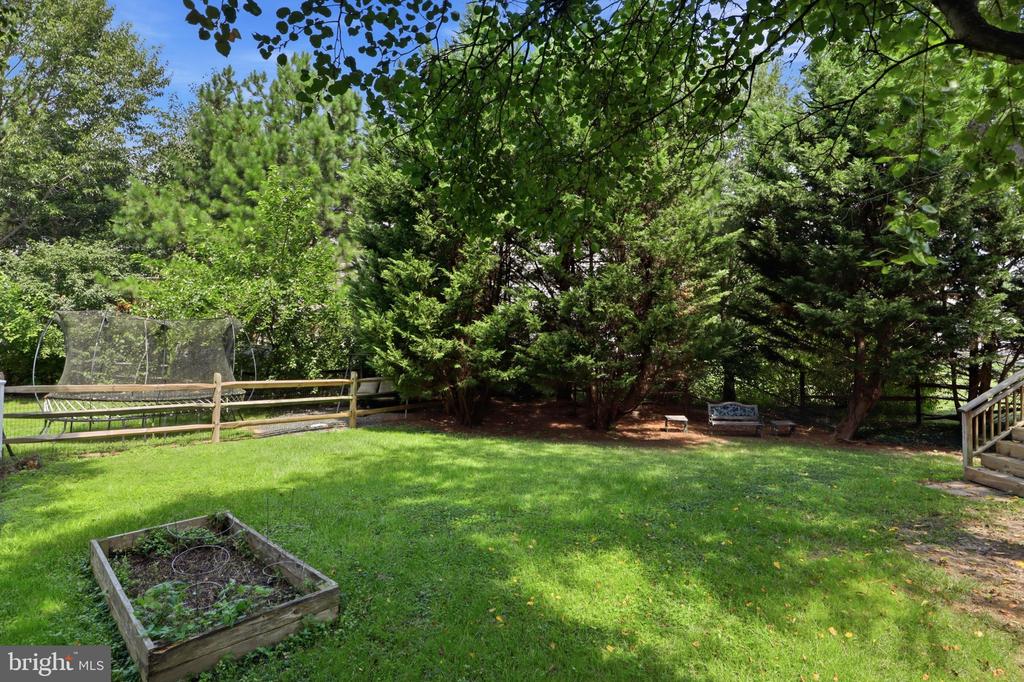 Backyard with a lawn, mature trees, raised garden bed, trampoline, and small seating area.