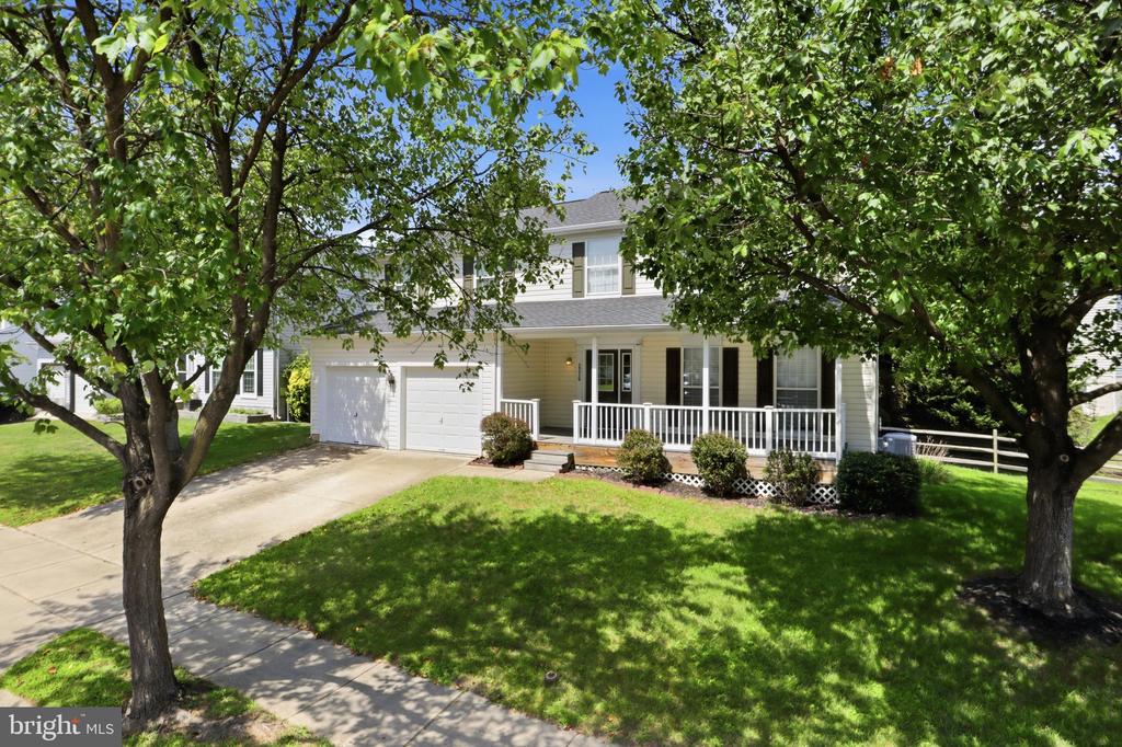 Two-story house with a double garage and covered porch, framed by mature trees and a green lawn.