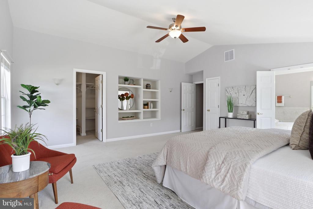 Furnished bedroom with built-in shelves, a ceiling fan, and a red chair beside the bed.