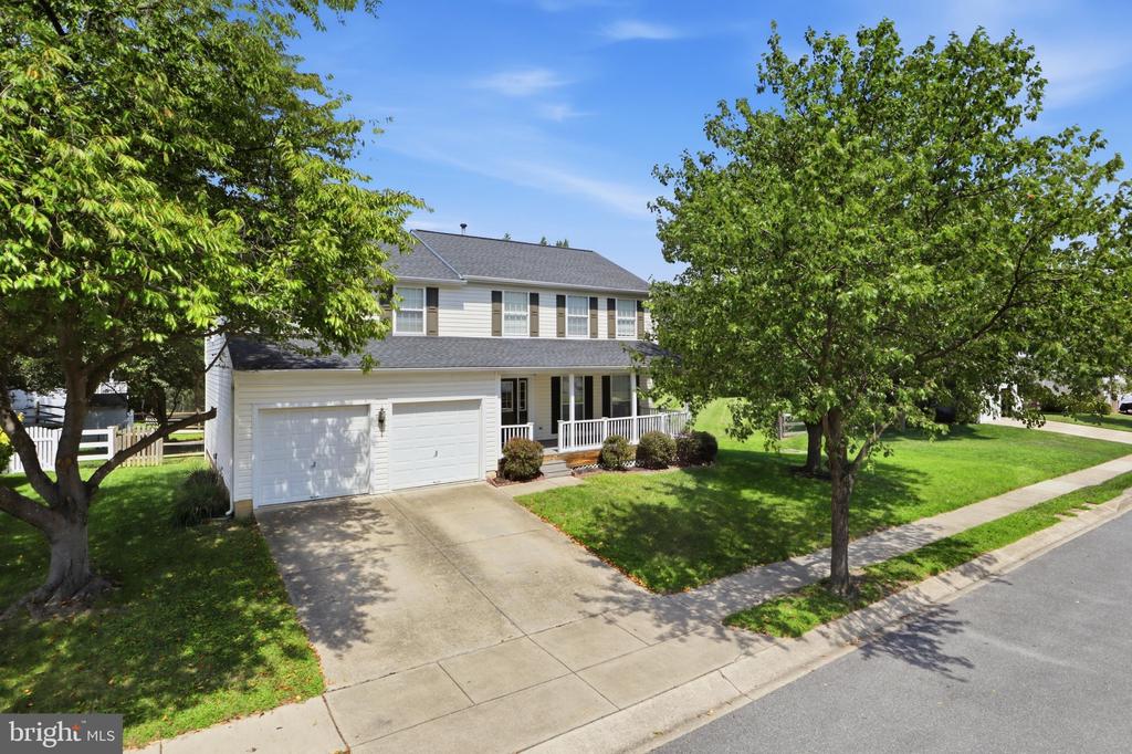 Two-story white-sided home with a two-car garage and covered porch, framed by mature trees.