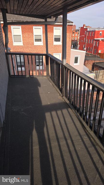 Covered balcony with black railings overlooking neighboring red-brick rowhouses.
