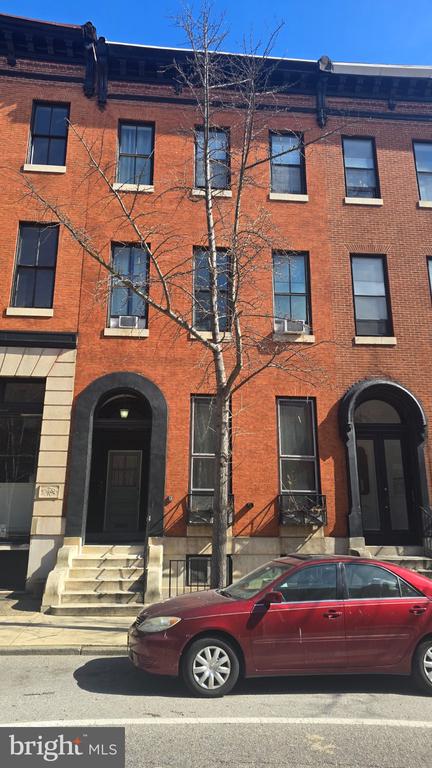 Red-brick rowhouse facade with arched entrances and a leafless street tree.