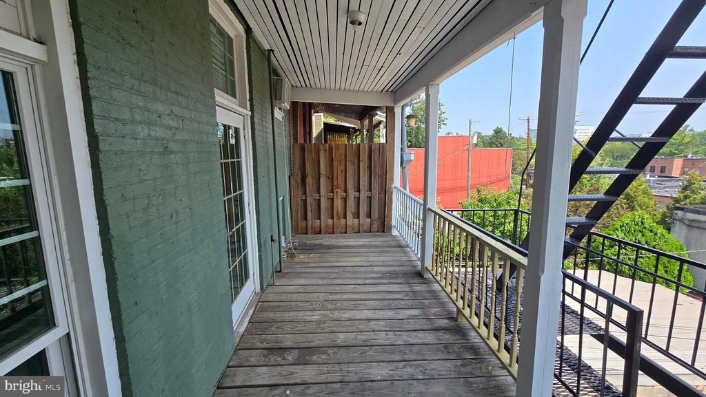 Covered wooden balcony with green brick walls, white railing, and an exterior metal staircase.