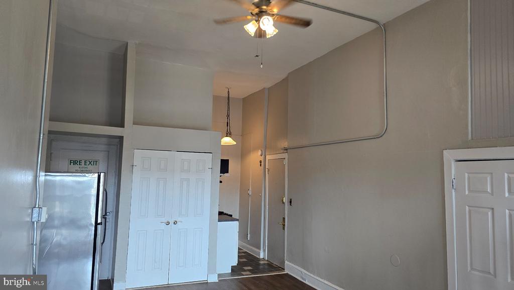 Vacant apartment interior with high ceilings, a ceiling fan, double closet doors, and a glimpse of the kitchen.