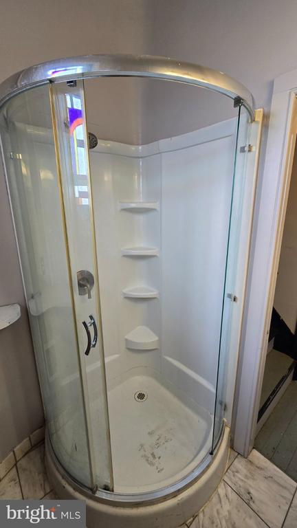 Bathroom corner shower with curved glass enclosure, built-in shelves, and marble-look floor.