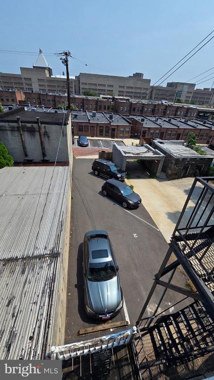 Rear parking area with parked cars, neighboring brick buildings, and a metal fire escape.