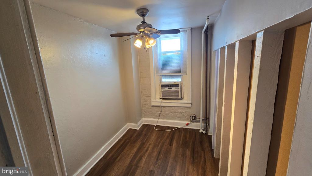 Vacant narrow room with dark wood floors, a ceiling fan, and a window air conditioner.